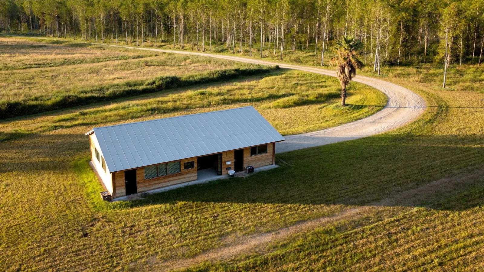 Aerial view of a detached outbuilding on a rural Florida property with a long gravel driveway curving through open grass
